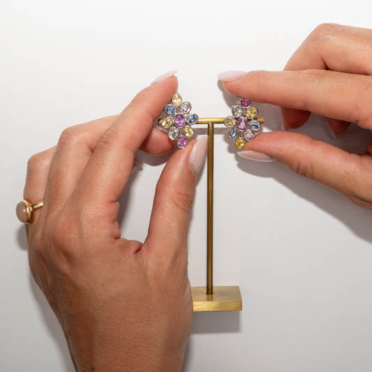 Hands holding a pair of multi color sapphire earrings on a white background