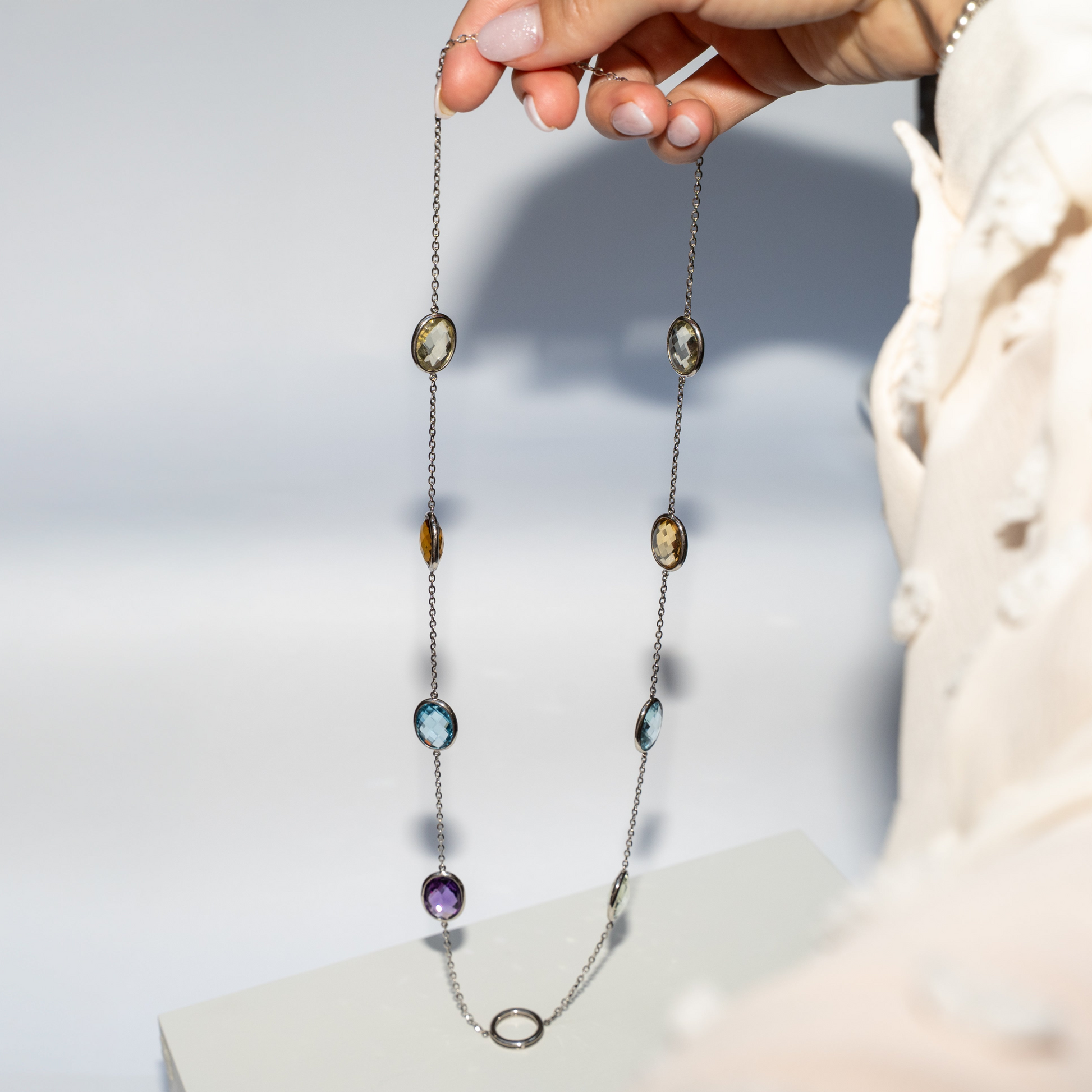 Colorful Necklace Oval Gemstones set in white gold with hand on light grey background