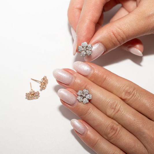 Flower-shaped diamond earrings on a hand with a white background