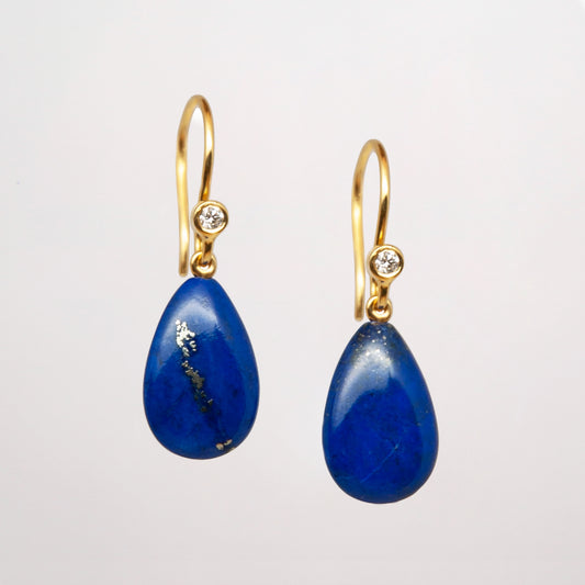 Pair of lapis lazuli gold earrings with blue teardrop stones and diamonds on a grey background