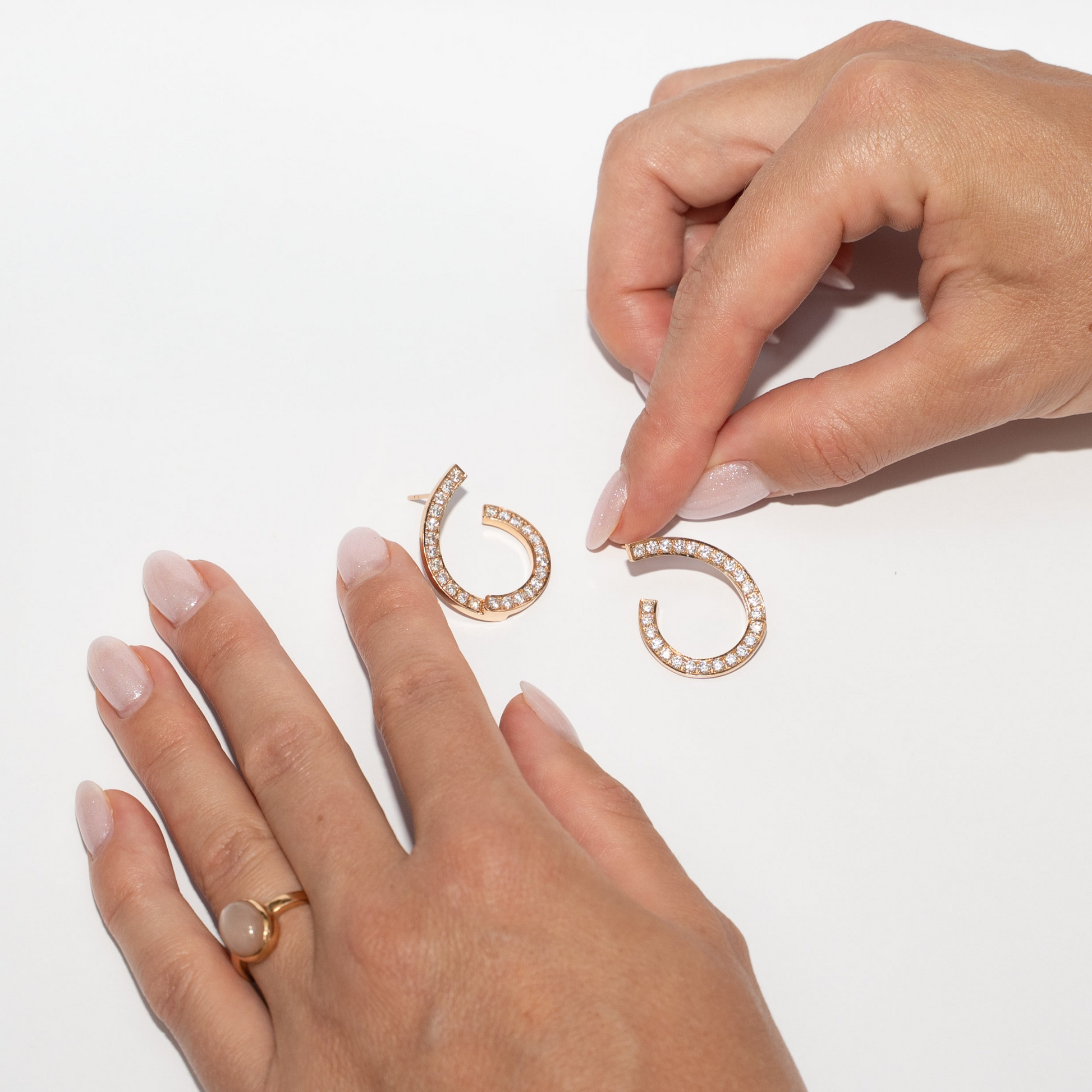 Rose gold hoop earrings with diamonds on a white background with hands